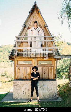 Die Braut steht auf dem Balkon eines dreieckigen Hauses, über dem Bräutigam, der auf dem Bürgersteig steht Stockfoto