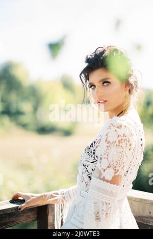 Mädchen in einem weißen Korbkleid steht mit der Hand auf einem hölzernen Handlauf Stockfoto