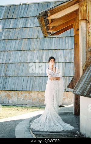 Die Braut im Korbkleid steht an der Schwelle eines Holzhauses Stockfoto
