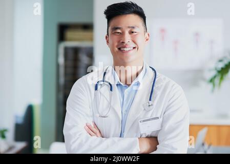 Ich bin zuversichtlich, dass ich mich um Euch kümmern kann. Beschnittenes Porträt eines jungen männlichen Arztes, der mit gefalteten Armen in einem Krankenhaus steht. Stockfoto