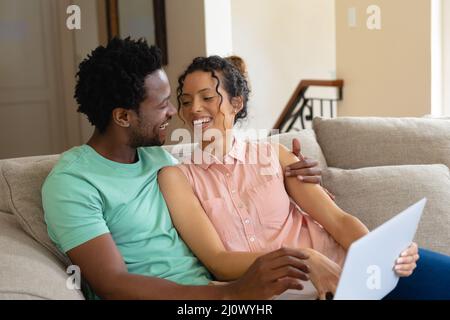 Glückliches junges biracial Paar mit Laptop, während zusammen auf dem Sofa zu Hause sitzen Stockfoto