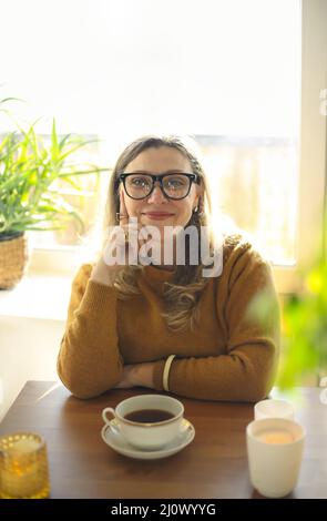 Porträt einer Frau mittleren Alters mit einer Tasse Tee, die mit brennenden Kerzen am Tisch sitzt Stockfoto