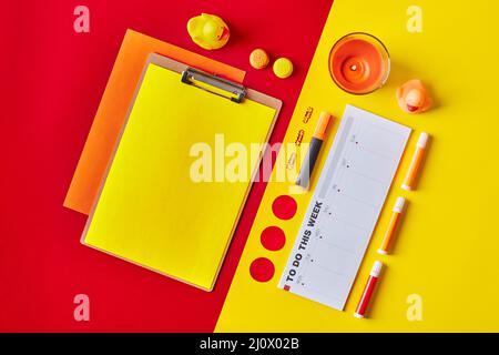 Papier auf Klemmbrett mit Planer, Kerzen, Papeterie in rot-gelben Farben. Flatlay-Arbeitsplatz Stockfoto