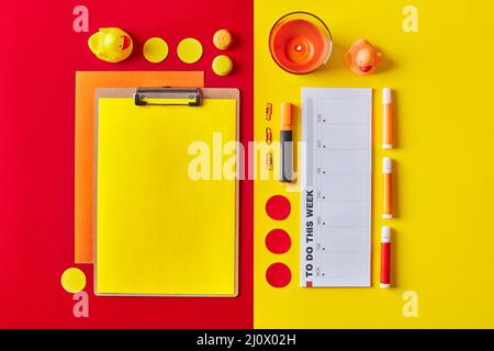Papier auf Klemmbrett mit Planer, Kerzen, Papeterie in rot-gelben Farben. Flatlay-Arbeitsplatz Stockfoto