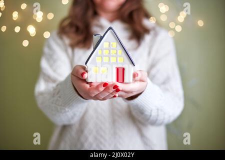 Frau hält in ihren Händen Keramikhaus mit Licht im Inneren. Das Konzept von Urlaub, weihnachten und Gemütlichkeit Stockfoto