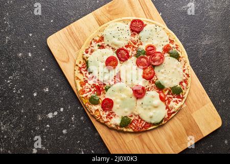 Fastfood gebackene Tiefkühlpizza mit Käse, Tomaten und Pesto. Bereit zum Essen. Stockfoto