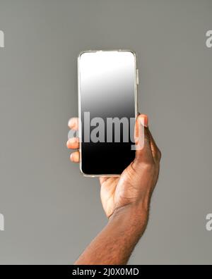 afroamerikanischer Mann hält Smartphone mit schwarzem Bildschirm an der Kamera. Gesperrter Bildschirm Smartphone in afrikanischen Mann Hand isoliert auf gr Stockfoto