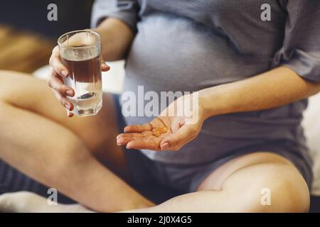 Schwangerin, die während der Schwangerschaft pränatale Vitamine einnahm und dabei Wasserglas und Pille in den Händen hielt Stockfoto