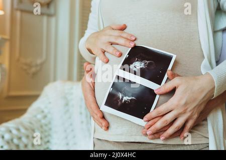 Familienplanung. Der liebevolle Ehemann umarmte seine schwanger Frau und hielt Ultraschalluntersuchungen in den Händen Stockfoto