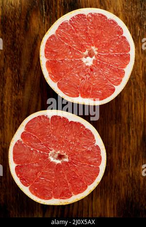 Zwei Hälfte rote Grapefruit, helle Kreise auf dunklem Holzhintergrund. Zitrusfrüchte Stockfoto