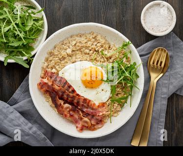 Haferflocken, Spiegelei und gebratener Speck. Brutales Männersportfrühstück. Herzhaftes fettreiches kalorienreiches Frühstück, Stockfoto