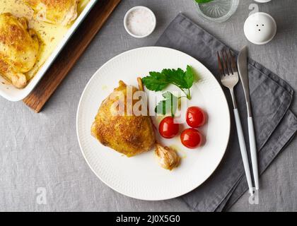 Hähnchenschenkel gebacken mit Kurkuma, Tomaten und Knoblauch. Gebratenes Huhn ist auf dem Teller Stockfoto