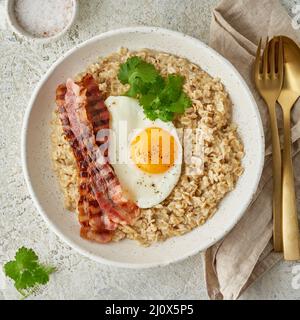 Haferflocken, Spiegelei, gebratener Speck. Herzhaftes, fettes, kalorienreiches Frühstück, Blick von oben Stockfoto