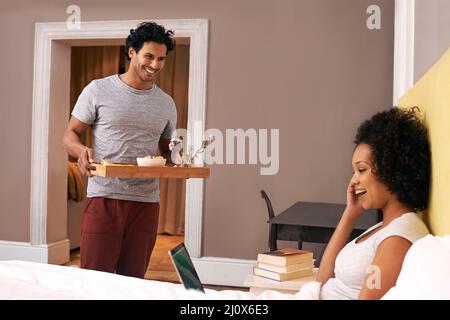 Überraschte sie beim Frühstück. Ein junger Mann bringt seine Freundin zum Frühstück ins Bett. Stockfoto