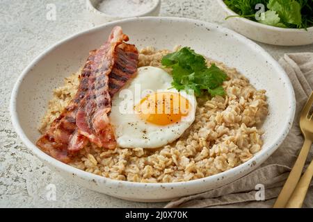 Haferbrei, gebratenes Ei, gebratener Speck. Herzhaftes fettes, kalorienreiches Frühstück. Gleichgewicht von Proteinen, Fetten, Kohlenhydraten, Seitenansicht Stockfoto