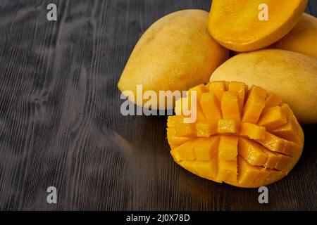 Vier ganze Mangofrüchte auf einem Holztisch und in Scheiben geschnitten. Große gelbe Früchte, Kopierraum Stockfoto