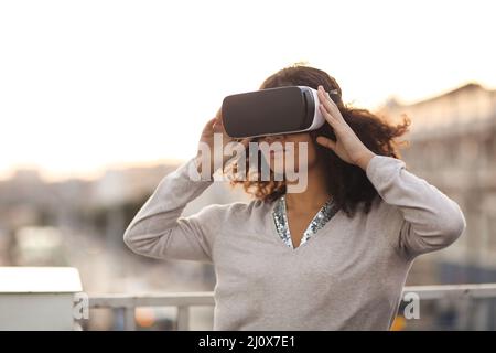 Junge, moderne Frau mit gemischter Rasse im VR-Brillen-Headset, die die virtuelle Realität im Freien erkundet Stockfoto