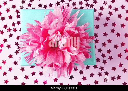 Blaue Geschenkbox aus Kraftpapier mit rosa Schleife auf rosa Hintergrund mit Konfetti. Weihnachtsgeschenk, valentinsüberraschung, Geburtstagskonzept. Flach liegend Stockfoto