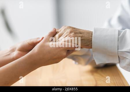 Krankenschwester, die die Hände des älteren Mannes hält, tröstet. Hochwertiges, schönes Fotokonzept Stockfoto