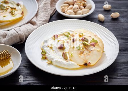 Ricotta mit Birnen, Pistazien und Honig oder Ahornsirup auf zwei weißen Teller auf dunkel Stockfoto