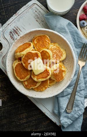 Pfannkuchen, Müsli, winzig dünne, lustige Krümel, Kinderessen. Frühstück mit Getränk, dunkler Tisch Stockfoto