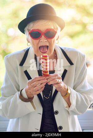 Ihr inneres Kind sucht nach Eis. Porträt einer lebenslustigen älteren Frau, die draußen ein Eis isst. Stockfoto