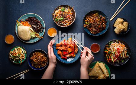 Set mit chinesischen Gerichten auf dem Tisch, weibliche Hände mit Essstäbchen Stockfoto