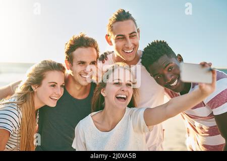 Feiern Sie die Sommersaison mit einem Selfie. Aufnahme einer glücklichen Gruppe von Freunden, die zusammen Selfies am Strand machen. Stockfoto