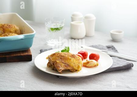 Hähnchenschenkel gebacken mit Kurkuma, Tomaten und Knoblauch. Gebratenes Huhn ist auf dem Teller Stockfoto