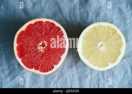 Zwei Hälften aus roter und weißer Grapefruit, helle Kreise auf dunkelgrauem Leinenhintergrund Stockfoto