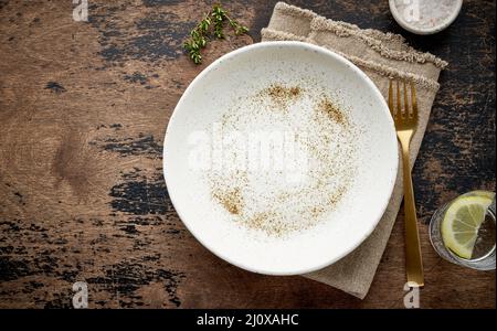 Leere weiße Keramikplatte, Gabel und Messer auf braunem, dunklem, altem Tisch reinigen, Platz für Kopien schaffen, nach oben verspotten Stockfoto