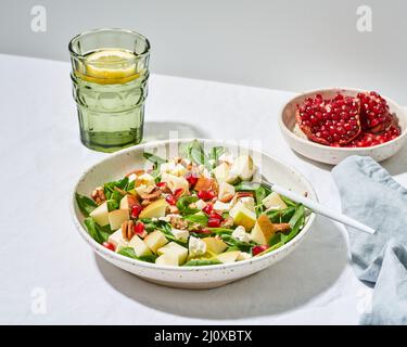 Pinach mit Äpfeln, Pekannüssen und Feta, garniert mit Granatapfelkernen in einer Schüssel auf dem Tisch Stockfoto
