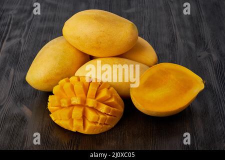 Vier ganze Mango-Früchte auf Holztisch und in Scheiben geschnitten. Große saftige leuchtend reife gelbe Früchte Stockfoto