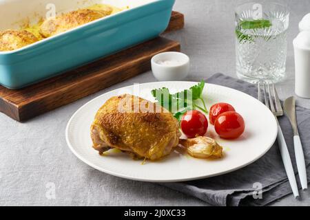 Hähnchenschenkel gebacken mit Kurkuma, Tomaten und Knoblauch. Gebratenes Huhn ist auf dem Teller Stockfoto