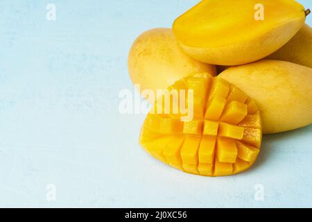 Vier ganze Mango-Früchte auf hellblauem Tisch und in Scheiben geschnitten. Große saftige gelbe Früchte Stockfoto