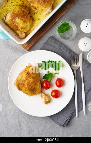 Hähnchenschenkel gebacken mit Kurkuma, Tomaten und Knoblauch. Gebratenes Huhn ist auf dem Teller Stockfoto