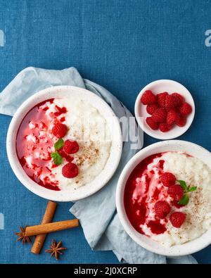 Reispudding. Französisches Milchdessert mit Himbeeren. Blaues Textil. Draufsicht, vertikal, Kopierbereich Stockfoto