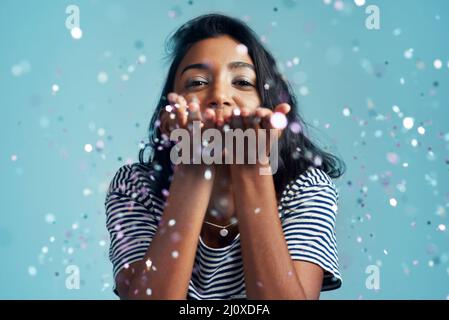 Wählen Sie, was Sie glücklich macht. Ausgeschnittene Aufnahme einer schönen jungen Frau, die im Studio Konfetti bläst. Stockfoto