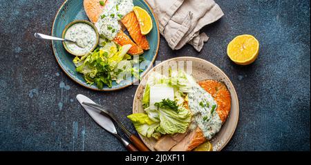 Gesundes Essen gegrillte Lachssteaks mit Dillsauce und Salatblättern auf zwei Tellern Stockfoto