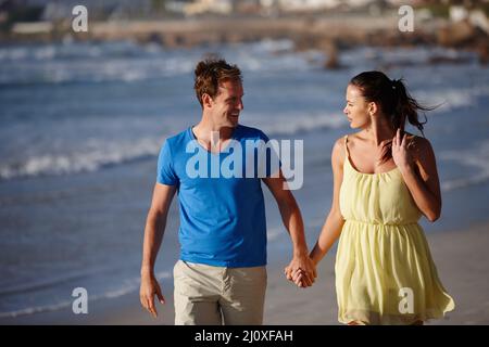 Hand in Hand und von Angesicht zu Angesicht. Aufnahme eines liebevollen Paares, das am Strand spazierenging. Stockfoto