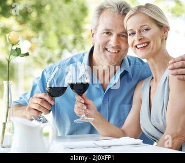Immer noch verliebt und einander verpflichtet. Glückliches reifes Paar, das seine Liebe mit zwei Gläsern Wein im Freien toaste. Stockfoto