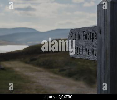 Hölzerner Straßenschild mit 'Public Footpath Lodge 1,5 ML' darauf, der zum Pfad zu einem Ufer führt Stockfoto