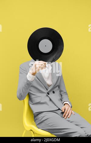 Mann, der sein Gesicht mit Vinyl-Schallplatten bedeckt, während er ultimative graue Kleidung trägt. Hochwertige Fotos Stockfoto