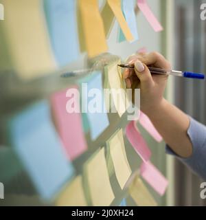 Frau schreibt Haftnotizen Bürofenster. Hochwertige Fotos Stockfoto