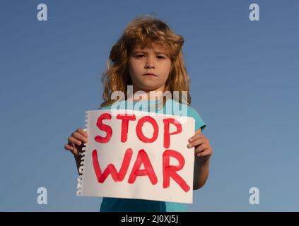 Kind trägt ein Schild Krieg stoppen. Portrait kleiner Junge ruft zu stoppen Krieg, hebt Banner mit Inschrift stoppen den Krieg. Kind in einem Protest mit ukrainisch Stockfoto