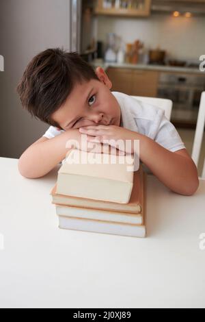 Müde und gelangweilter kleiner Junge, der sich auf Stapel- oder Schulbücher lehnte und auf die Kamera schaute Stockfoto