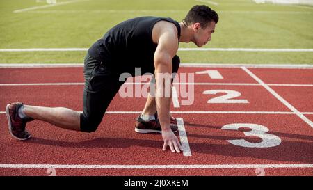 Seitenansicht der Sprinter des männlichen Läufers bereitet sich auf das Rennen vor. Hochwertige Fotos Stockfoto