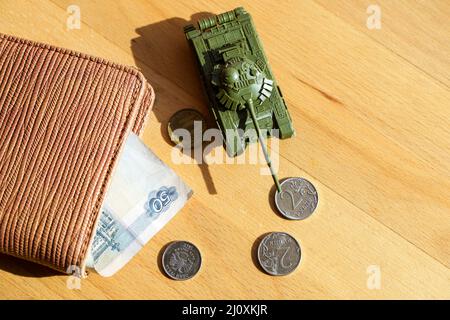 Krieg in der Ukraine und Sanktionen gegen Russland Konzept. Geldbörse mit russischen Rubel und einem Spielzeugtank auf dunklem Hintergrund. Wirtschaftskrise, Zahlungsausfall, Zusammenbruch des Rubels. Hochwertige Fotos Stockfoto