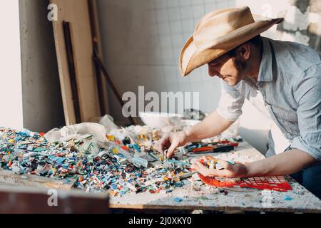 Mann Mosaiken Meister wählt ausgewählte Smaltglasstücke für Mosaik-Panel. Männlicher Mosaikist bei der Arbeit. Stockfoto