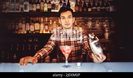 Männlicher Barkeeper macht roten Cocktail Gießen Alkohol aus Shaker Glasbar Hintergrund. Stockfoto